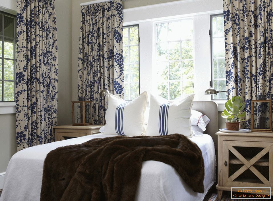 Niebieskie kwiaty na zasłonach i paskach na poduszkach harmonijnie łączą się we wnętrzu sypialni