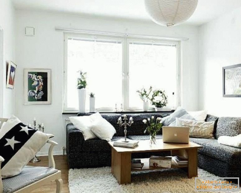 Mały salon w kolorze białym z ciemną narożną sofą i oknem