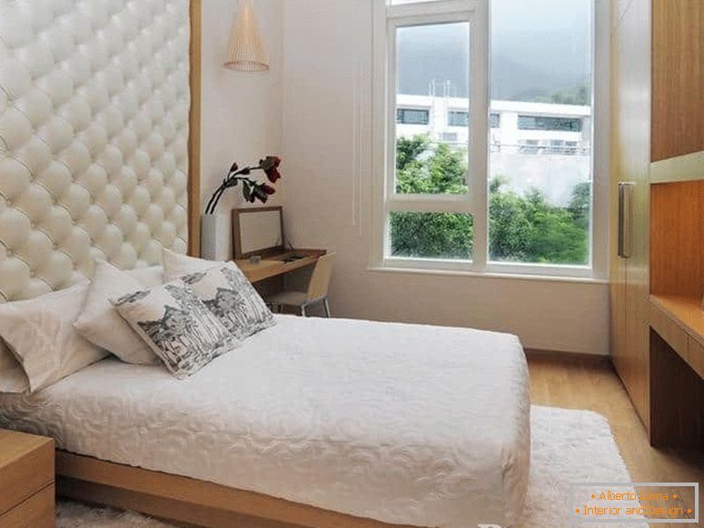 Małe łóżko ze skórzanym zagłówkiem oraz w sypialni z dużym oknem