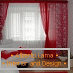 Czerwone zasłony, poduszki i dywan w połączeniu z białymi ścianami i meblami