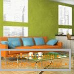 Pomarańczowa kanapa z błękitnymi poduszkami przeciw pistacja ściany tłu