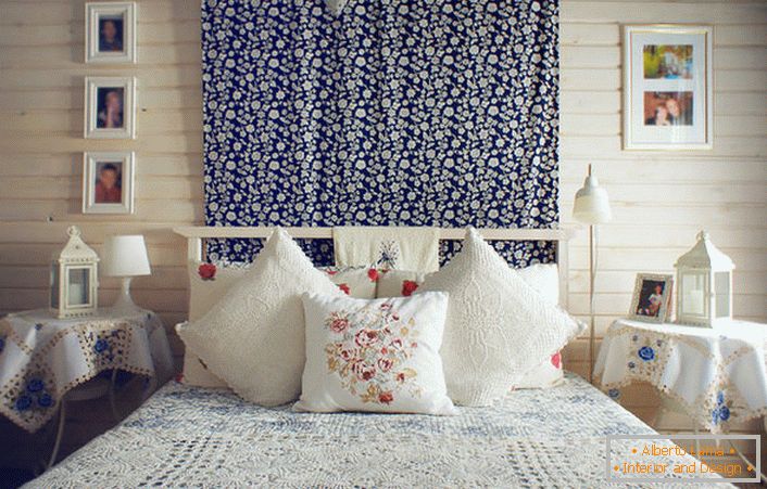 W stylu rustykalnym łóżko zdobią liczne poduszki z kontrastującymi czerwonymi haftami. Stoliki nocne pokryte są obrusem z delikatnymi niebieskimi kwiatami.