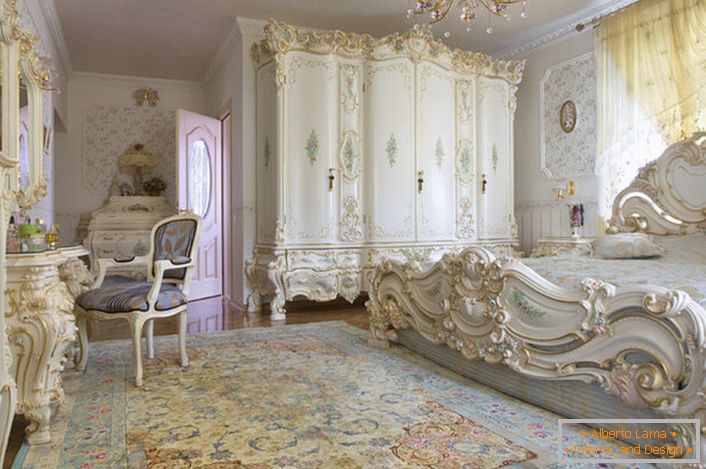 Śnieżnobiała sypialnia z rzeźbionymi masywnymi meblami z drewna. Łóżko z wysokim zagłówkiem przy zagłówku, elegancko pasuje do wnętrza w stylu barokowym.