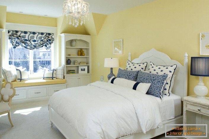 Wyblakły żółty kolor wykończenia harmonizuje z biało-niebieskim elementem wystroju. Niezwykła kombinacja to odważne rozwiązanie dla sypialni w wiejskim stylu.