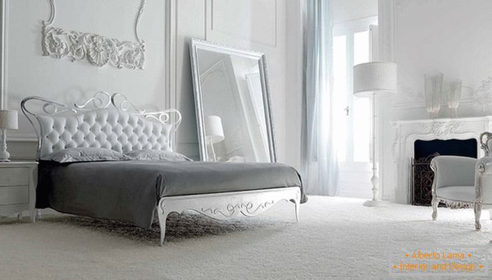Ściana u wezgłowia łóżka ozdobiona jest dekoracyjną sztukaterią. Białe wnętrze wyróżnia niezwykłe szerokie lustro w prostej, lakonicznej ramie.