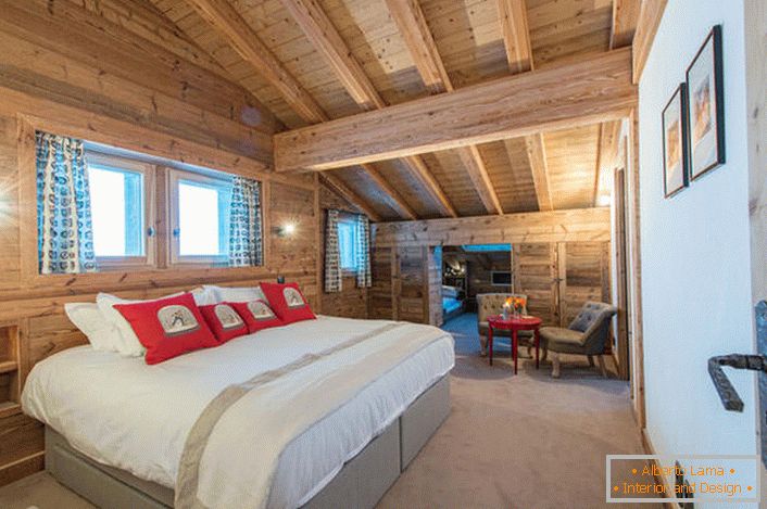 Przestronna sypialnia na drugim piętrze wiejskiej rezydencji z drewnianego domu z bali. В соответствии со стилем кантри искусственный свет в комнате приглушен. 