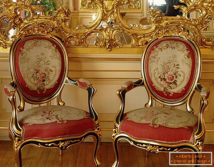 Ażurowa sztukateria ze złotym kolorem na lustrze i krzesłami z czerwoną miękką tapicerką - jaskrawymi przedstawicielami stylu barokowego.