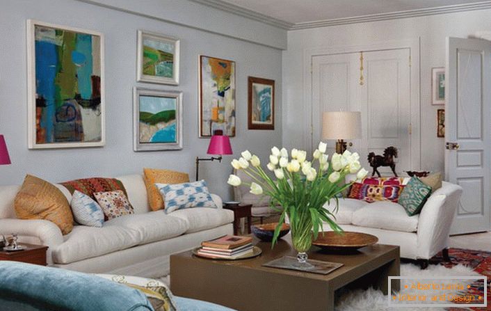 Uniwersalny salon w eklektycznym stylu. Przytulny pokój ma wiele poduszek i abstrakcyjnych, jasnych obrazów zdobiących ścianę nad sofą.