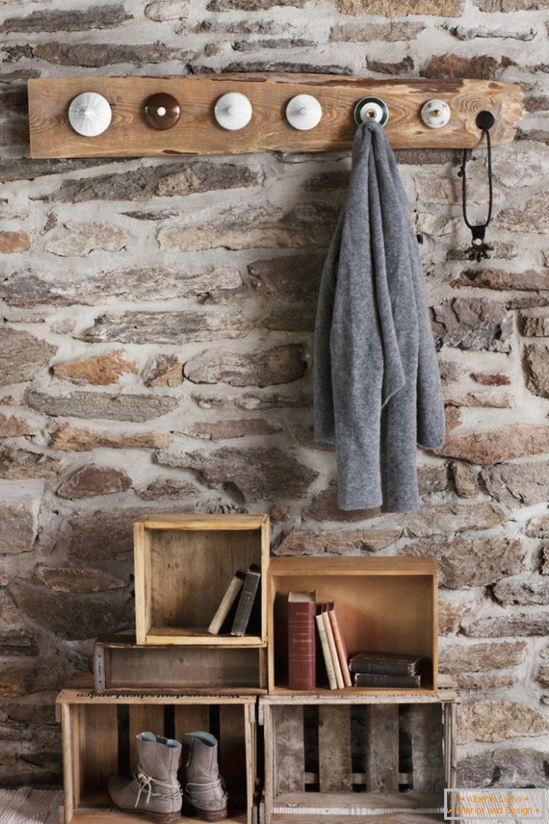 Rustykalny DIY szatnia w pokoju z kamiennym murem; wieszaki wykonane ze starych porcelanowych pokrywek i stare drewniane skrzynie na podłodze jako magazyn