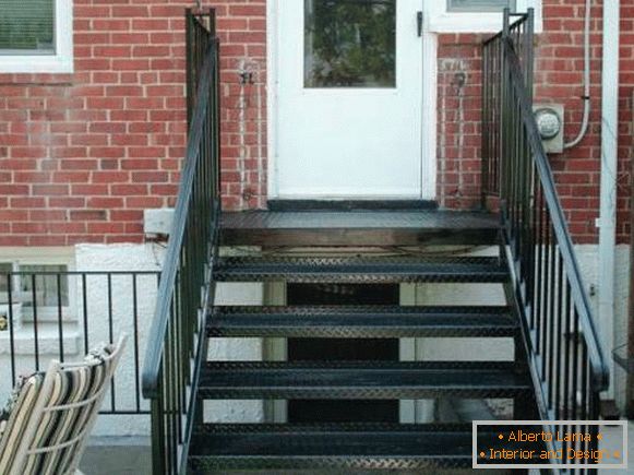 Mały metalowy ganek ze schodami prowadzącymi do domu z cegły