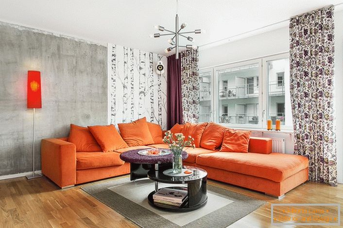 Skandynawski styl wpisany jest w ciepłe kolory w wystroju wnętrz. Miękka pomarańczowa kanapa wygląda naturalnie na tle ścian o zimnym szarym odcieniu.