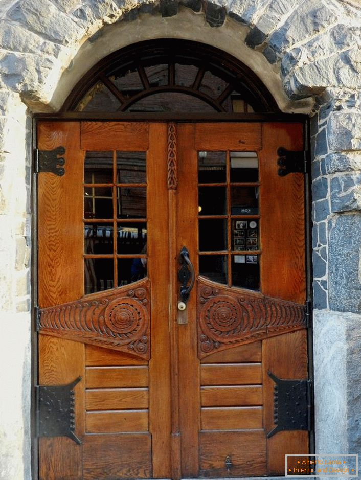 Drzwi w secesyjnym stylu zdobią drzwi wejściowe wiejskiej chaty z fasadą z naturalnego kamienia. 