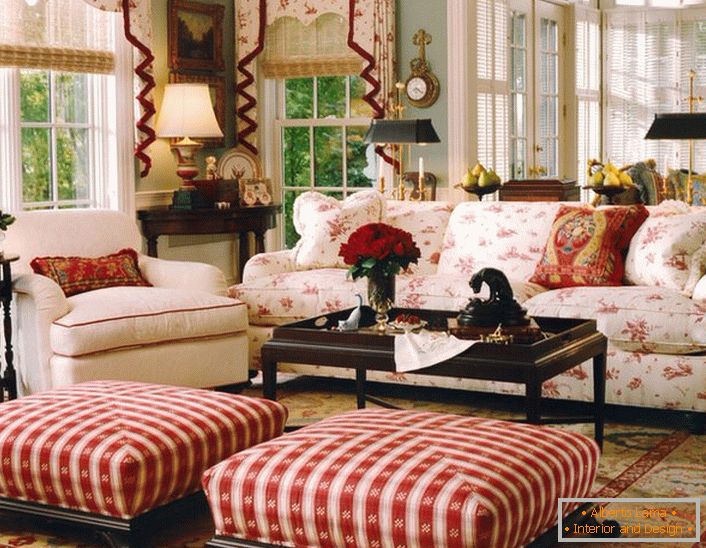 Prosty, skromny i przytulny salon w stylu angielskim w małym wiejskim domu. Akcenty czerwieni sprawiają, że atmosfera w pokoju jest rozluźniona i wesoła.
