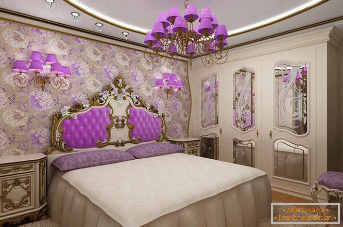 Elegancka barokowa sypialnia z ciekawym akcentem na oświetlenie. Żyrandol i lampki nocne z tymi samymi fioletowymi odcieniami harmonijnie połączonymi z tapicerką oparcia przy czole łóżka.